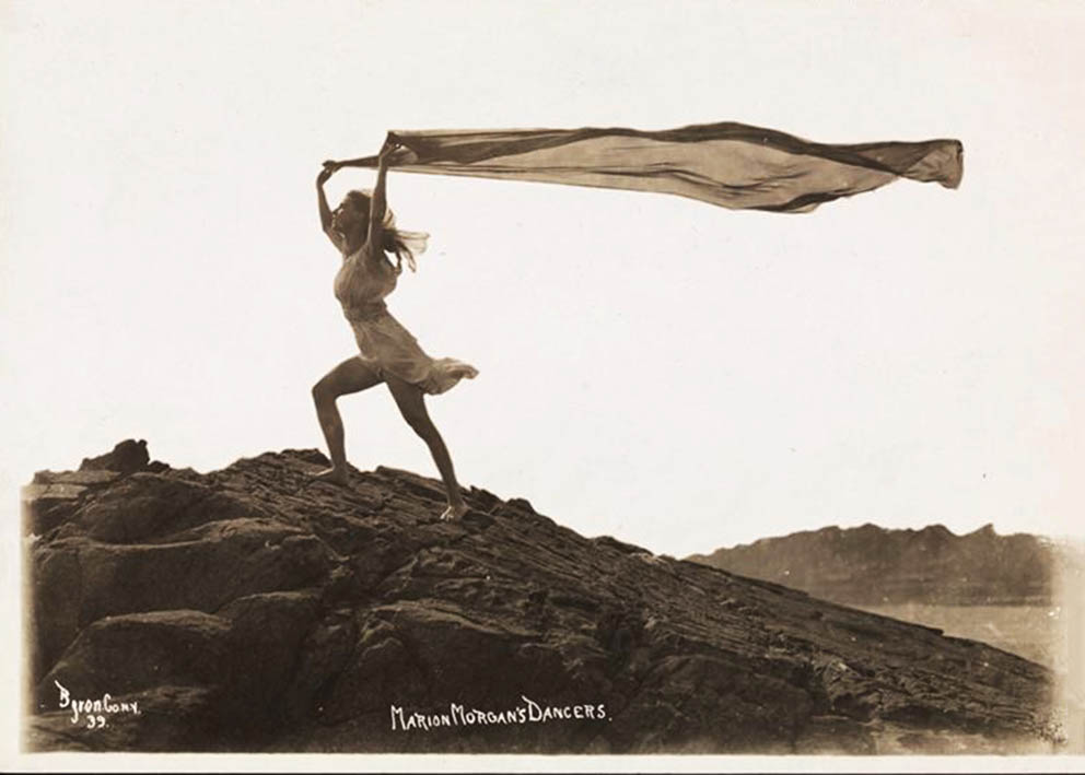 Byron Company - One of Marion Morgan's dancers with a long, diaphanous scarf flowing in the sea breeze, posing on rock at the beach Rye, New York. 1920